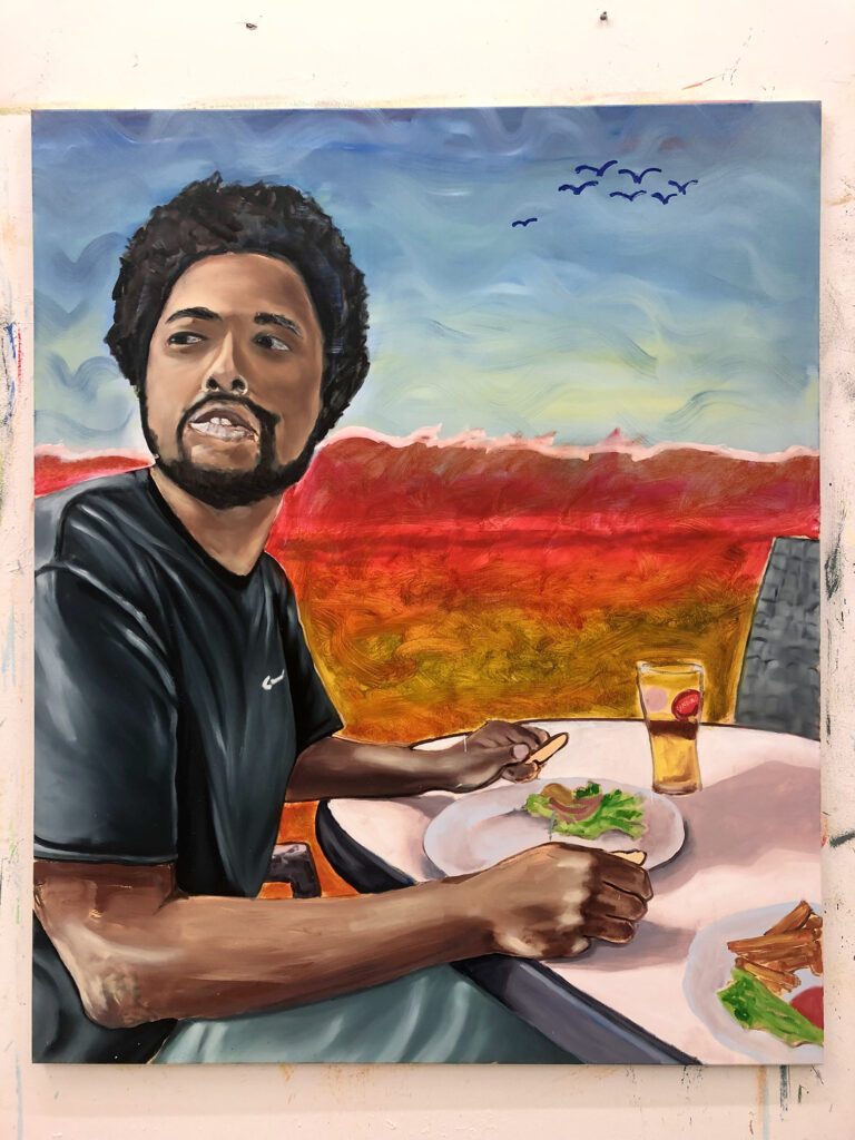 Das Gemälde Nordsee von Robin Rapp zeigt einen jungen farbigen Mann, der an einem Tisch sitzend einen Salat isst, im Hintergrund eine Landschaft aus rot-leuchtenden Dünen und einem Vogelschwarm