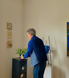 Älterer Mann richtet eine Blume im Wohnzimmer umgeben von Kunstwerken