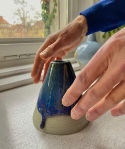 Zwei Hände, die sich einer kleinen Skulptur aus Keramik nähern