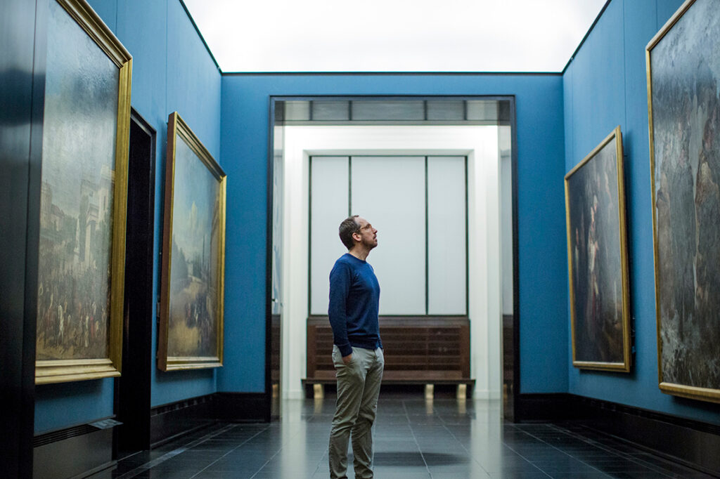Ein Mann steht in einer Gemäldegalerie und schaut sich alte Meister an