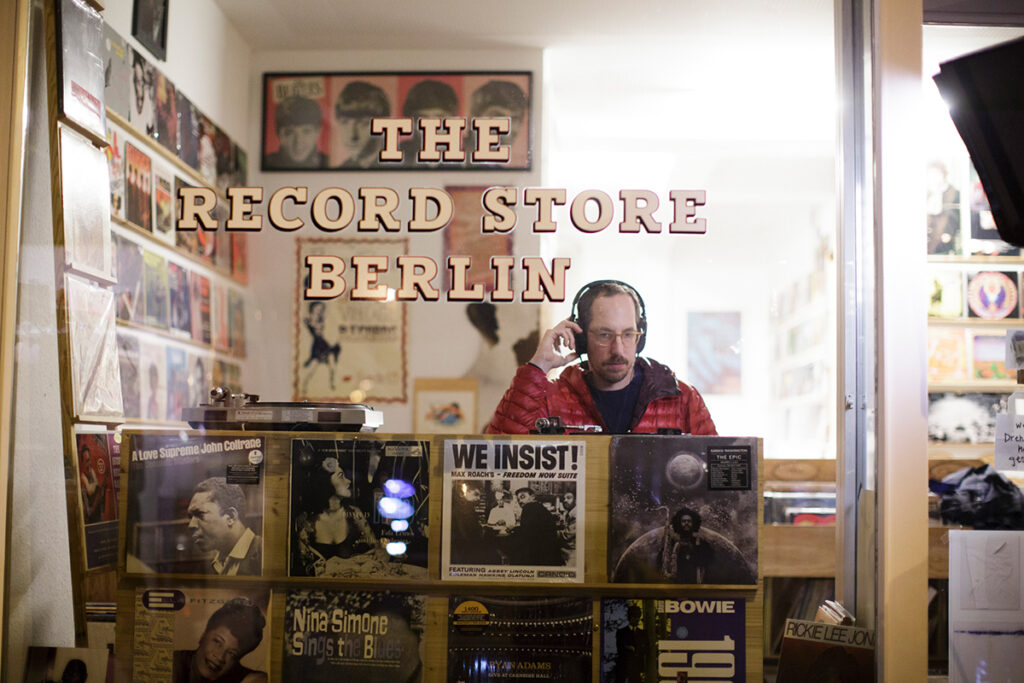 Ein Mann steht in einem Plattenladen mit Kopfhörern und hört Schallplatten.