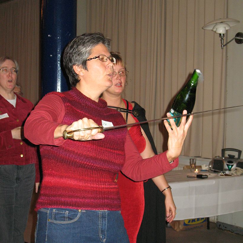Eine Frau öffnet mit einem Säbel eine Champagnerflasche