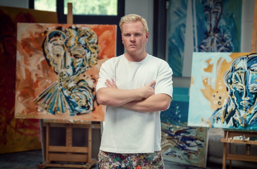 Das Bild zeigt Leon Löwentraut vor seinen Kunstwerken.
